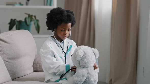 Serious African American Kid Girl Sitting in Room on Couch in Medical Uniform Pretending to Be