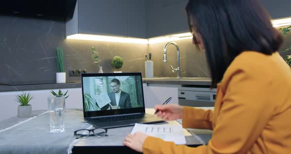 Woman Sitting in  Kitchen and Listening Explaining from Partner Via Video conference