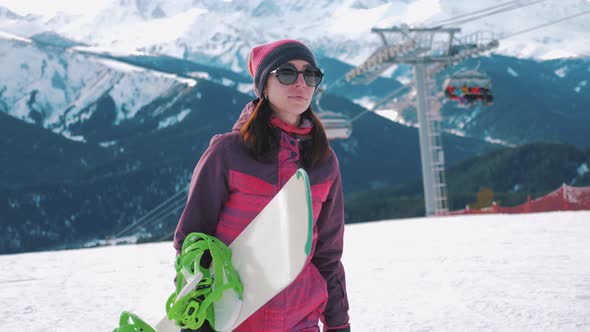 Girl Snowboarder Holding Snowboard in Hands at the Ski Resort. Sport Woman in Snowy Mountains. Sunny