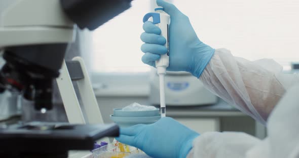 A Scientist in Sterile Clothing Looks Through a Microscope