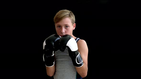 A Teenage Boxer in a Gray Sleeveless Shirt Holds His Hands in Gloves Near His Face