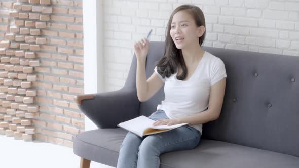 Beautiful young asian woman sitting on couch study and learning writing notebook at home.