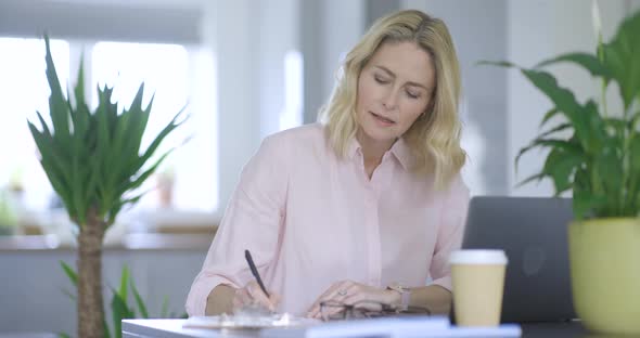 Blond businesswoman writing notes sitting at desk