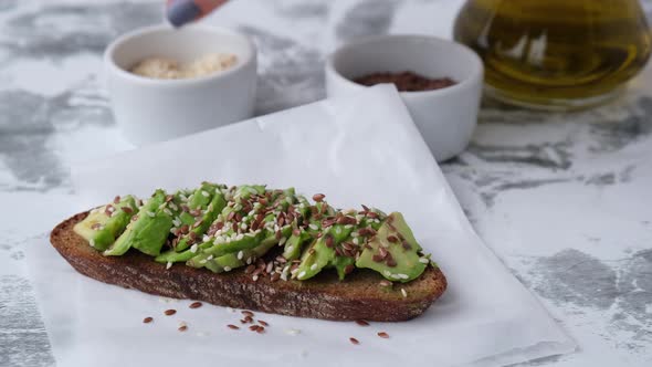 Female hand making Healthy avocado toast on wooden board. Sesame and flax seeds. Vegetarian food.