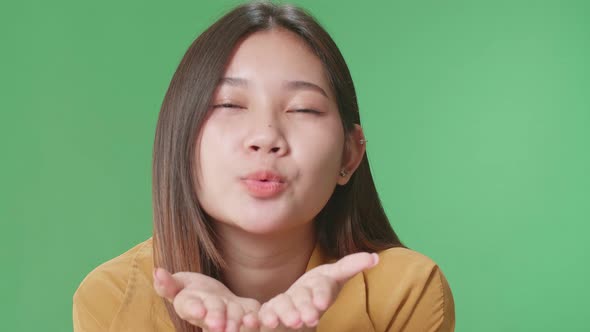 Portrait Of A Smiling Asian Woman Blowing Kisses To A Camera In The Green Screen Studio