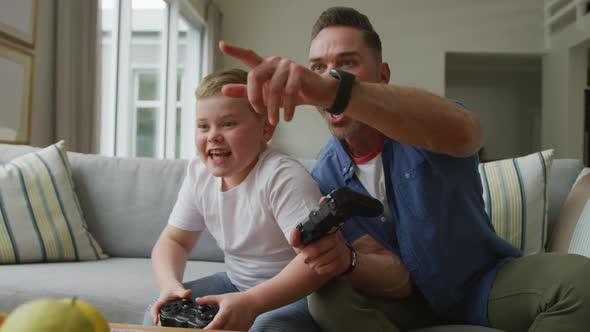 Happy caucasian father with son sitting in living room and playing video games