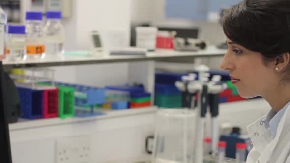 Female scientist looking at screen and tube in laboratory