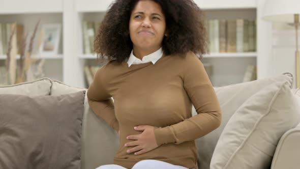 Young African Woman with Back Pain Sitting on Sofa