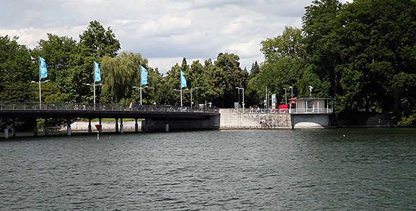 Bridge At Lake With Waving Flags, Cars And People