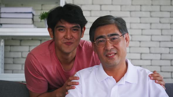 A portrait of son and senior father sitting on sofa at home.