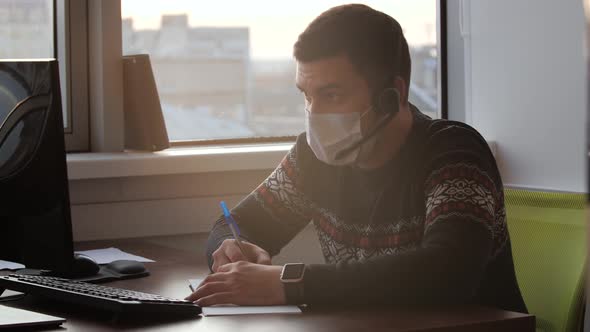 Caucasian Man Freelancer Wearing Medical Mask and Wired Headphones Working on Freelance From Home