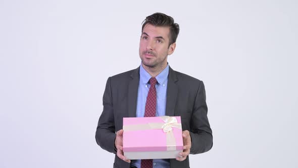 Young Happy Hispanic Businessman Thinking While Holding Gift Box