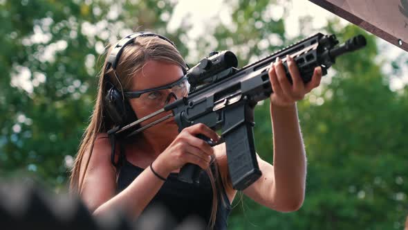 Young Caucasian Woman Wearing Protective Goggles and Headphones Practising with Submachine Gun on