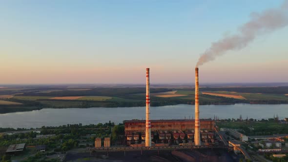 Manufacture near the river. Pipes with dirty smoke on nature background in the evening. 