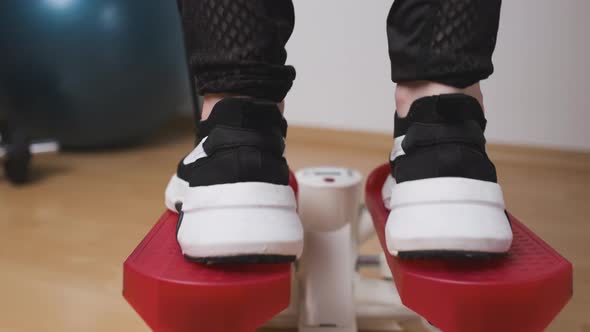 Back View of Female Legs Doing Exercises on the Twist Stepper in Sneakers and Sportswear at Home
