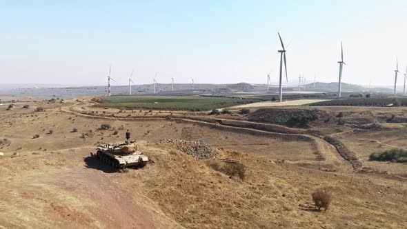 person standing on deserted tank looking at wind turbine farm landscape