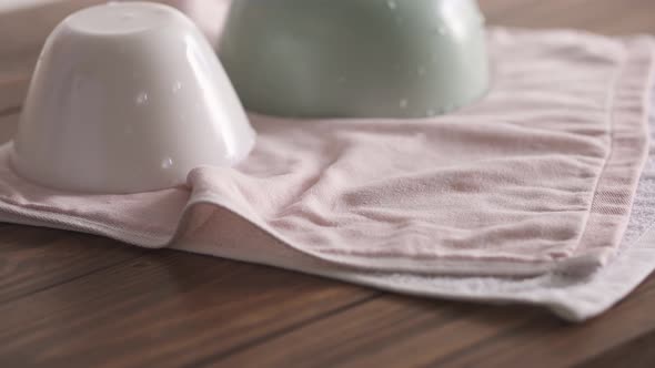 A Woman's Hand Puts A Wet Plate On A Towel. Clean Bowls On A Tea Towel. Kitchen In Elegant Pastel