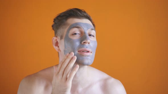 Young Man Applies a Gray Clay Mask To His Face, for Healthy Glowing Skin, Isolated Background