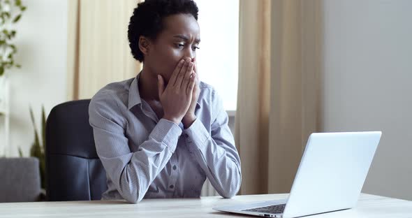 Shocked Stressed African American Woman Sitting at Table at Home or Office Looking at Laptop Screen