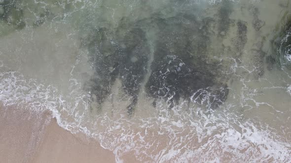 Top down aerial view of giant ocean waves crashing and foaming in coral beach