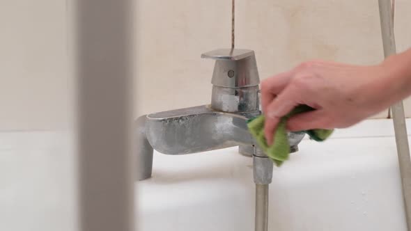 A Female Hand Cleans a Dirty Faucet with a Sponge and Detergent in the Bathroom