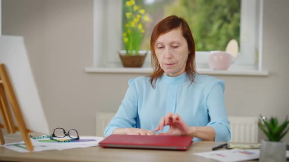 Portrait of Confident Intelligent Mature Freelancer Opening Laptop Putting on Eyeglasses Sitting at