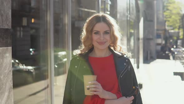 Stylish Beauty Smiles at the Camera While Standing on the Street Near a Modern Office Building