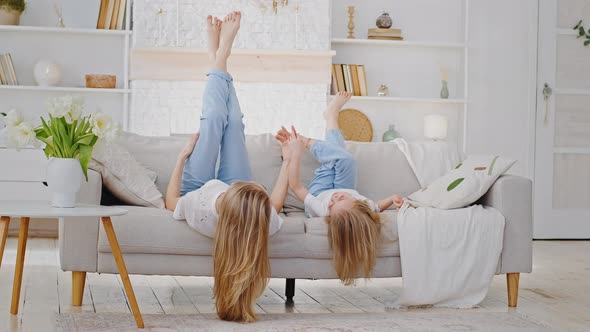 Mother and Small Daughter Caucasian Family Lie on Sofa in Living Room Upside Down with Legs Thrown