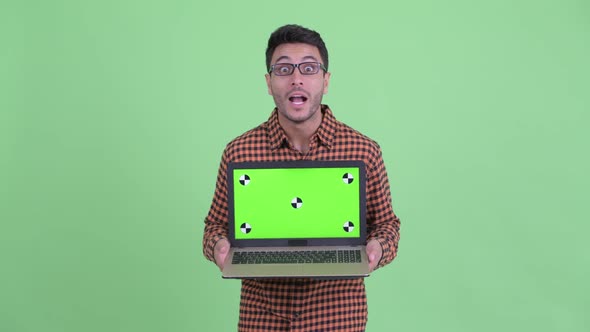 Happy Young Hispanic Hipster Man Showing Laptop and Looking Surprised