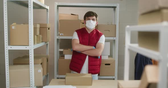 Man Wearing Red Vest Protective Gloves and Mask Employee of Warehouse Standing on the Background of