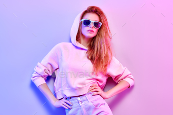 h hair, makeup on pink purple neon light. Redhead model in hoodie, fashion jeans, sunglasses. Beautiful girl in autumn fall neon style