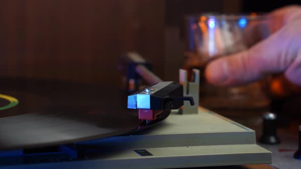 Hand Placing Gramophone Needle on Vinyl Record Taking Glass of Drink With Ice