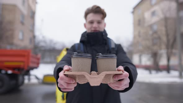 Blurred Young Courier Stretching Disposable Paper Coffee Cups at Camera Standing Outdoors on Cold