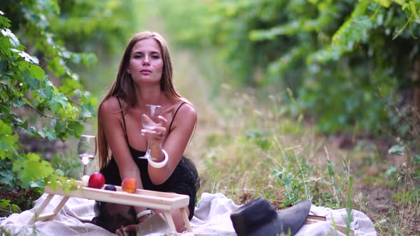 Beautiful Woman with Long Hair Drinks White Wine From a Glass at Sunset in the Vineyard