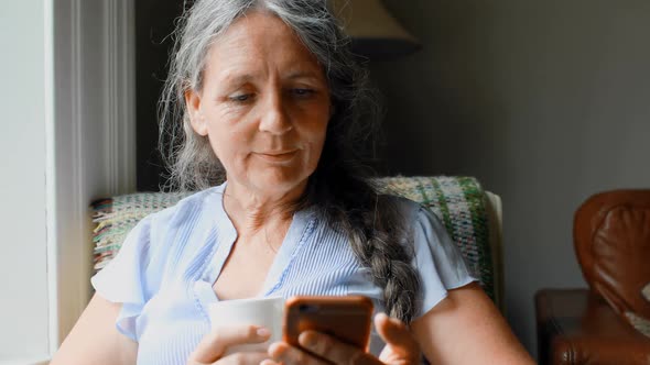 Senior woman having coffee while using mobile phone 4k