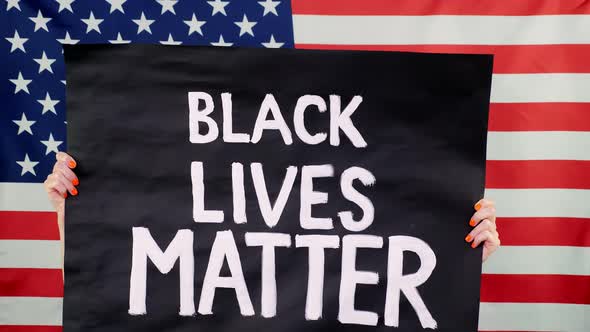 Protester Holds a Banner with a Slogan - Black Lives Matter - Against Background of the USA Flag