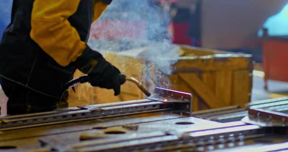 Closeup a Worker Welds Metal Parts Sparks Fly and Smoke Comes Out