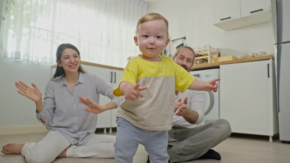 Caucasian baby boy child learn to walk, taking first step on floor with parents support in house.