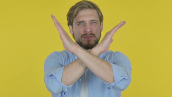 Rejecting Young Man with Arm Gesture on Yellow Background