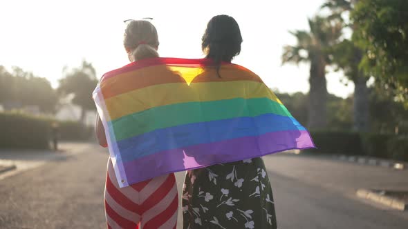 Back View of Two Slim Young Caucasian Women Walking with LGBT Flag in Slow Motion