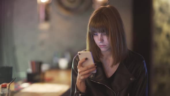 Young Beautiful Redhaired Woman Sitting in Cafe or Bar and Using a Smartphone