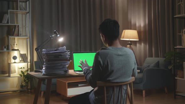 Back View Of Asian Man Talking To Green Screen Laptop While Working With Documents At Home