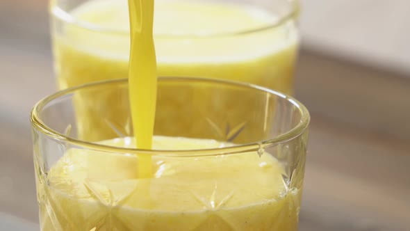 Tropical pineapple fruit smoothie drink being poured in to the glasses