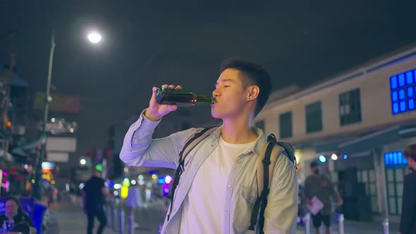 Asian handsome man traveler drink bottle of beer while walk on street.