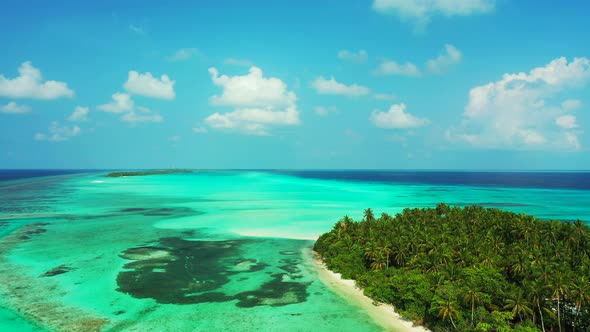 Wide angle fly over island view of a white sand paradise beach and blue sea background in 4K