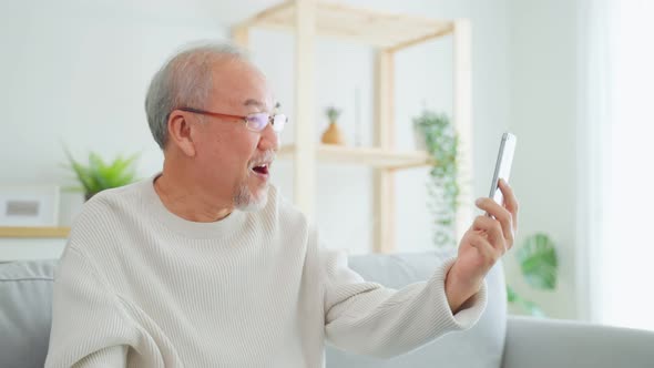 Asian senior older man use mobile phone for video call in living room.