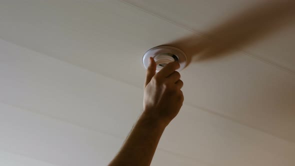 Men's Hand Tightening a Light Bulb in the Ceiling Then Lamp Turns on and Illuminates