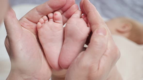 Mother Holds Tiny Pink Feet of Newborn Daughter on Bed