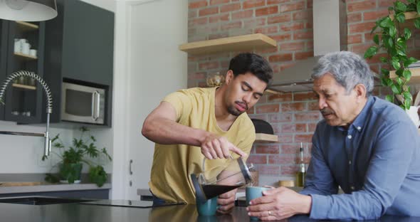 Young man pouring fresh black coffee in mug for father at kitchen counter