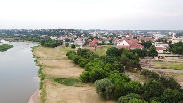 Kaunas castle and old town rooftops in distance ascending drone view
